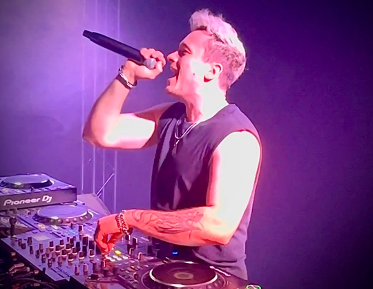 DJ mit Mikrofon auf Bühne beim SpringBeatz Festival, lila Lichtshow