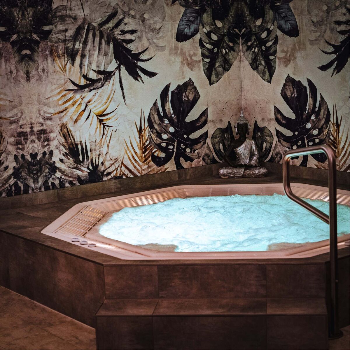 Beleuchteter Whirlpool mit Buddha-Statue vor tropischer Wandgestaltung im Relax Hotel