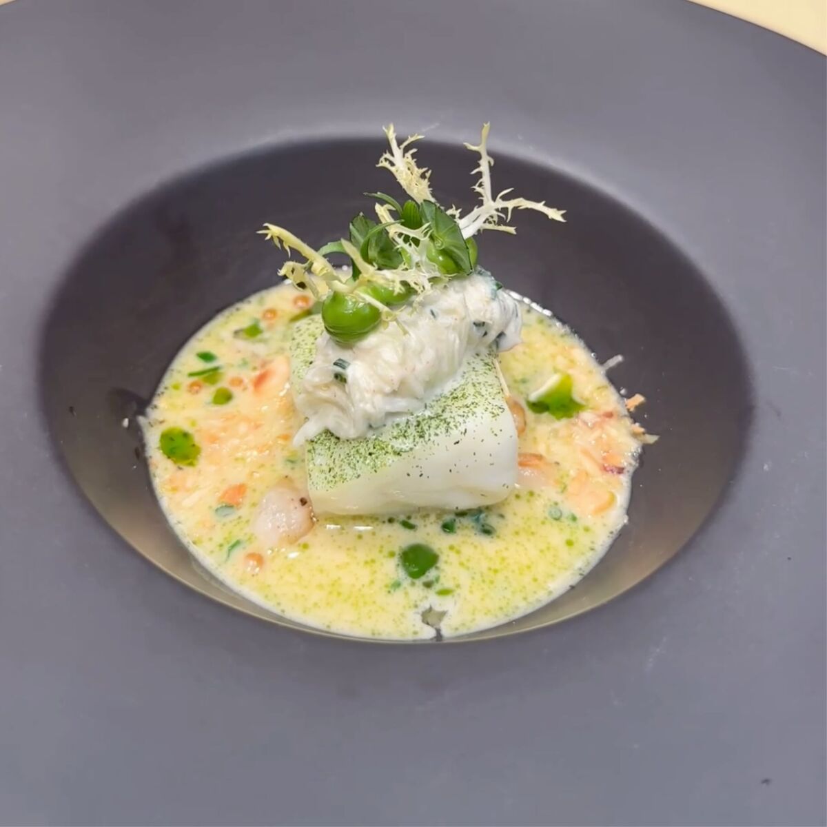 Fischfilet mit cremiger Sauce, Topping aus Gemüse und Kräutern auf schwarzem Teller